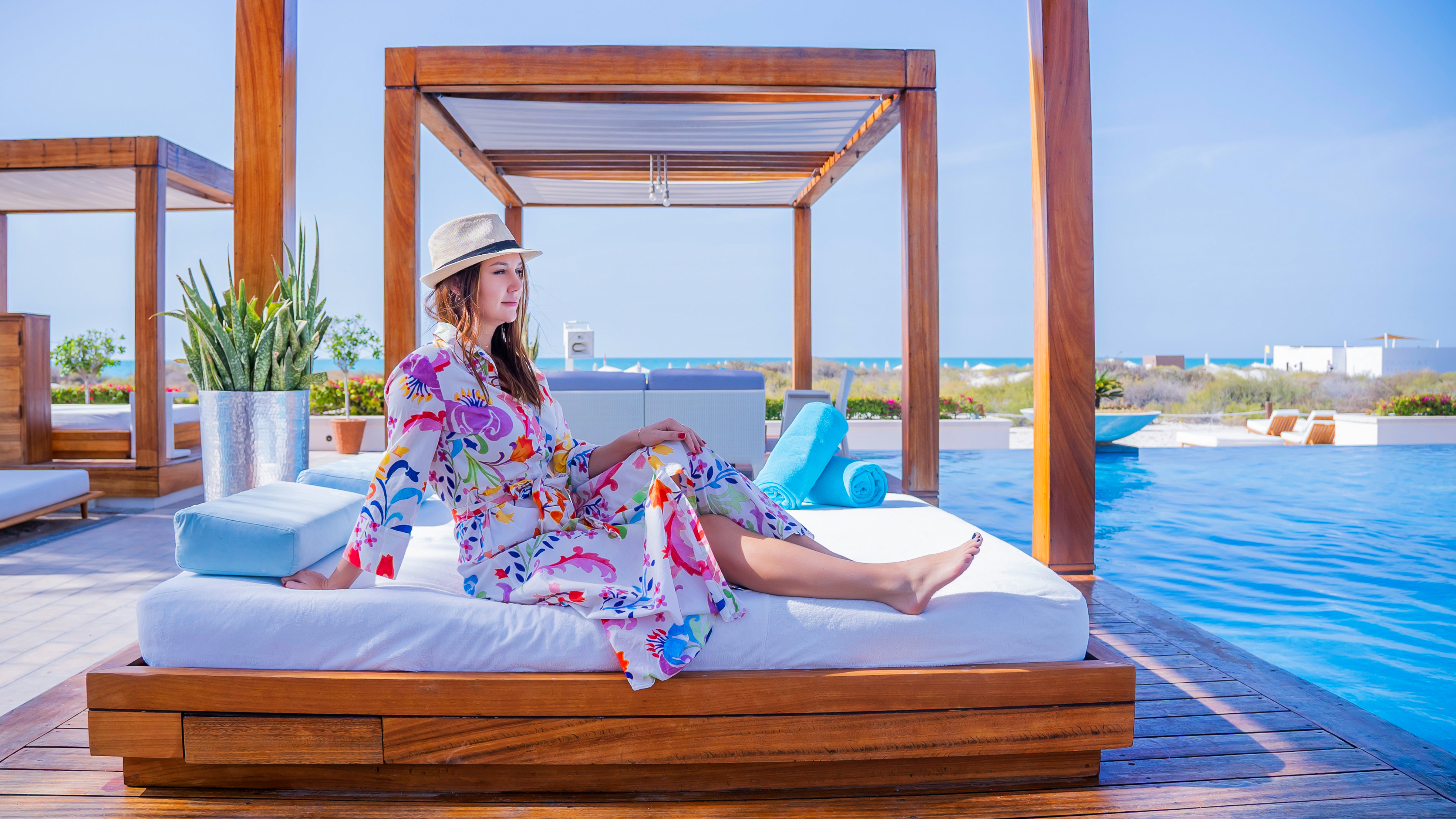 Woman lounging on a bed in a poolside cabana at Saadiyat Beach Club, enjoying a serene and stylish retreat.