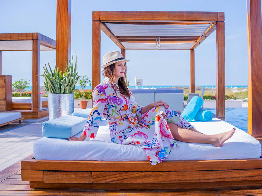 Woman lounging on a bed in a poolside cabana at Saadiyat Beach Club, enjoying a serene and stylish retreat.