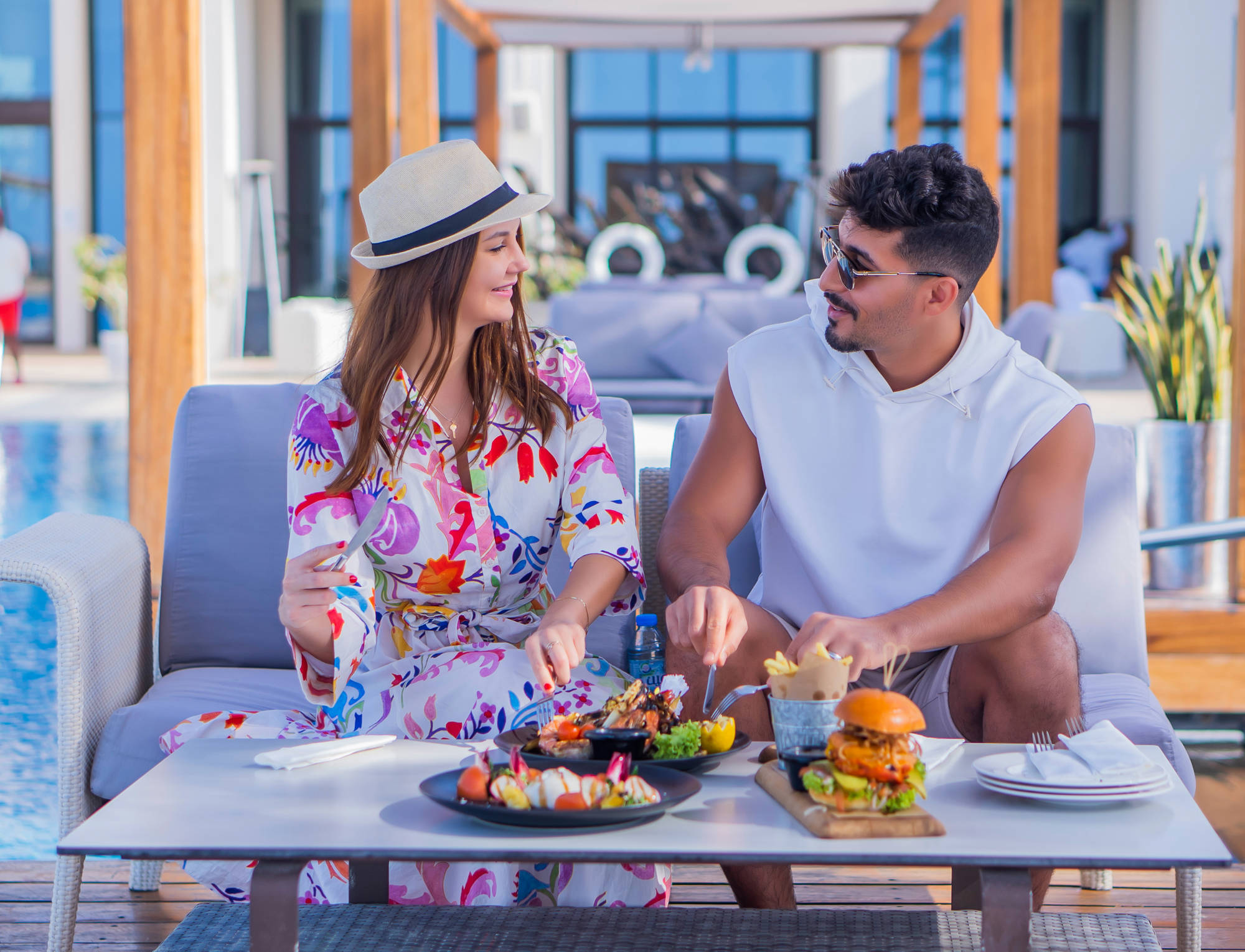 Couple enjoying alfresco dining at Saadiyat Beach Club, sharing a variety of dishes by the pool in a relaxed atmosphere.