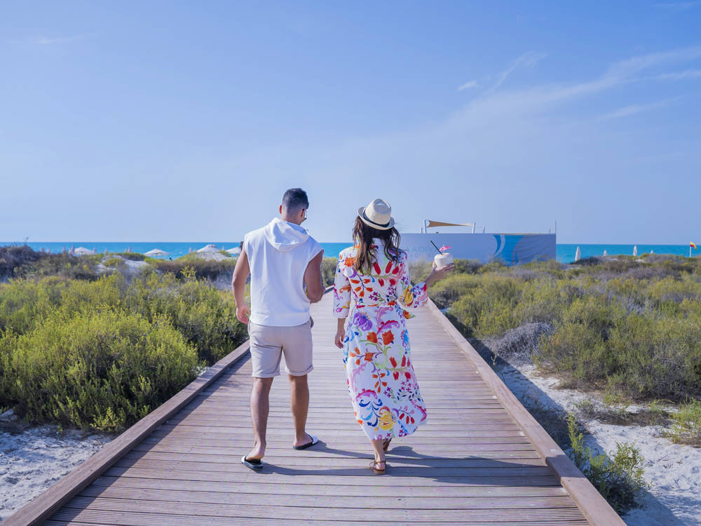 Strolling couple at Saadiyat Beach Club, framed by the calm sea and open horizon for a peaceful moment.