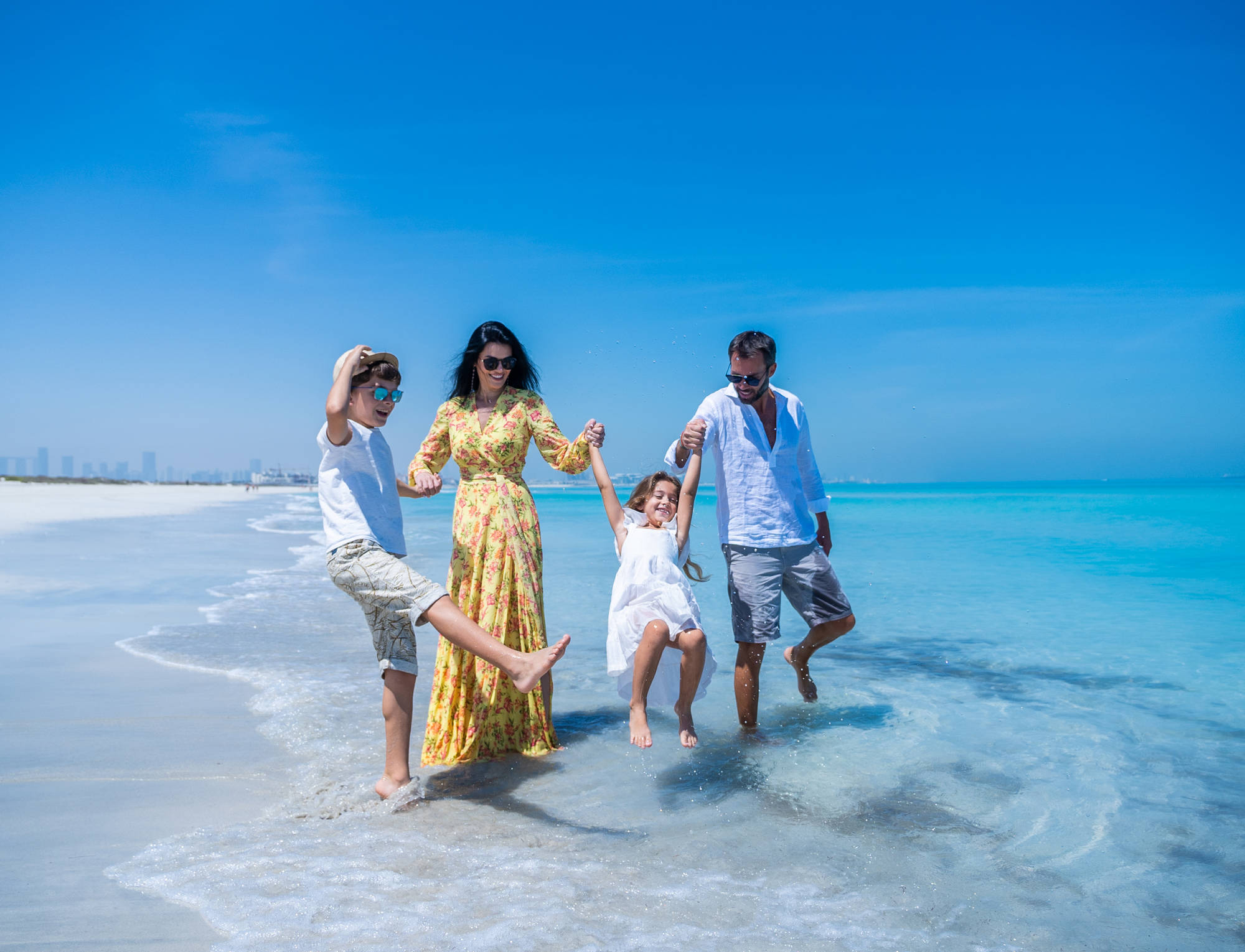 Carefree family enjoying beach time at Saadiyat Beach Club, splashing and playing together in the shoreline.
