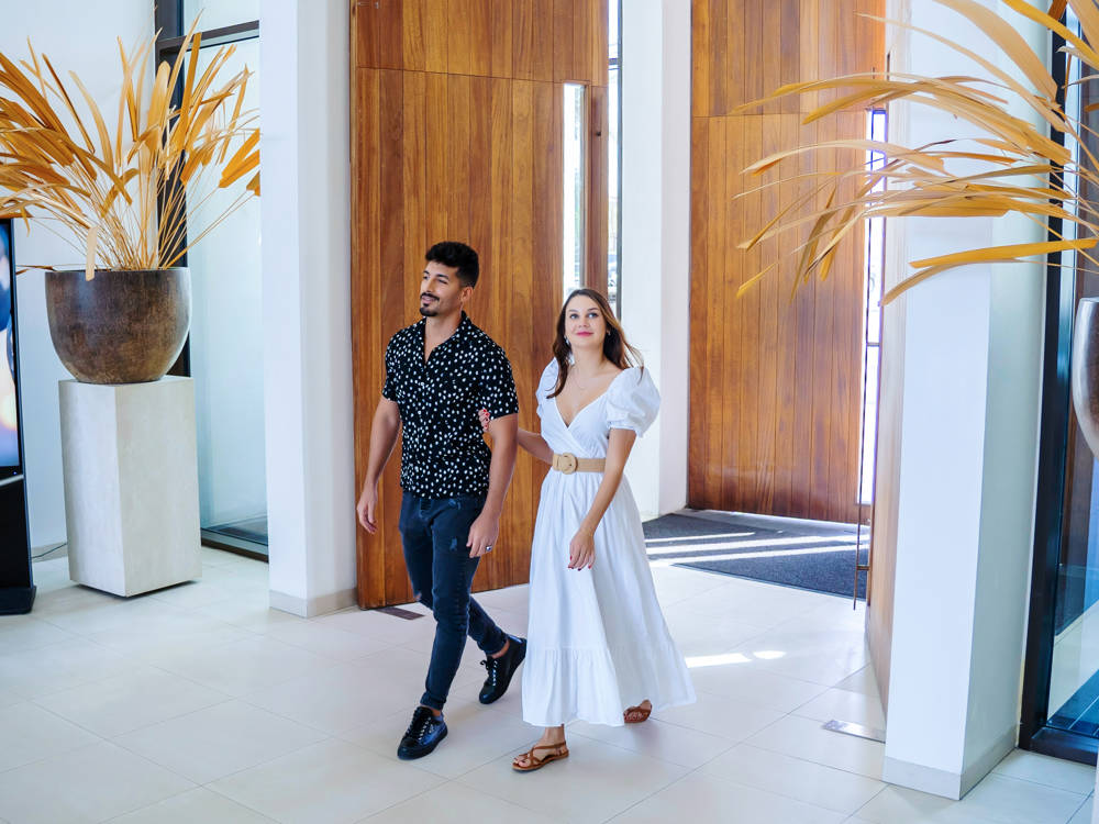 Couple strolling into Saadiyat Beach Club via a sunlit corridor, capturing a calm and welcoming arrival moment.